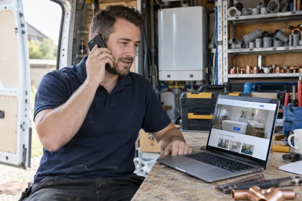 Tradesman taking a phone call with his new business website open on a nearby laptop